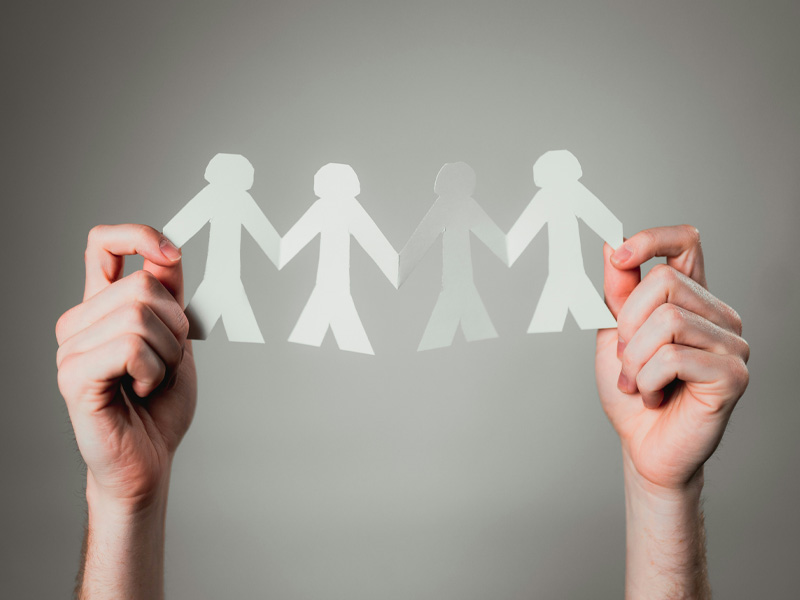 Hände halten ausgeschnittene Papierfiguren, die symbolisch für Gemeinschaft und Zusammenhalt stehen.
